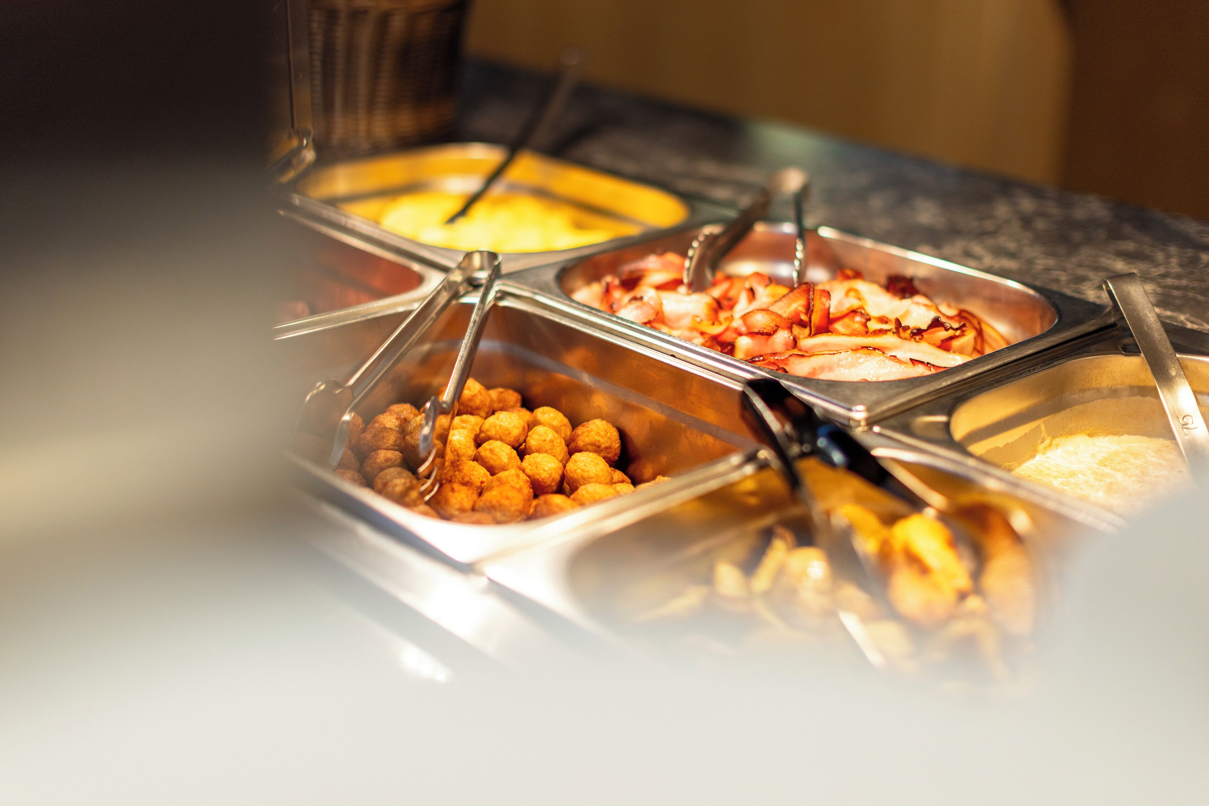 Un bufé con diversos alimentos en recipientes metálicos.