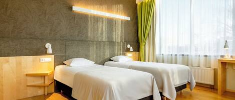 Habitación de hotel con dos camas, suelo de madera, un radiador y una ventana con cortinas.
