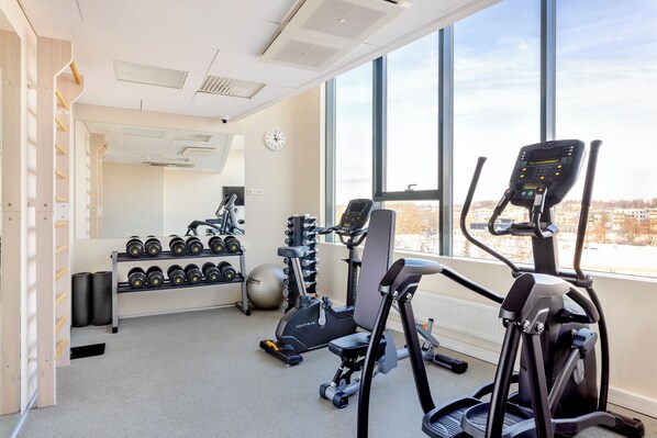 Un gimnasio con equipo de ejercicio, un soporte para mancuernas y un amplio ventanal con vistas a la ciudad.