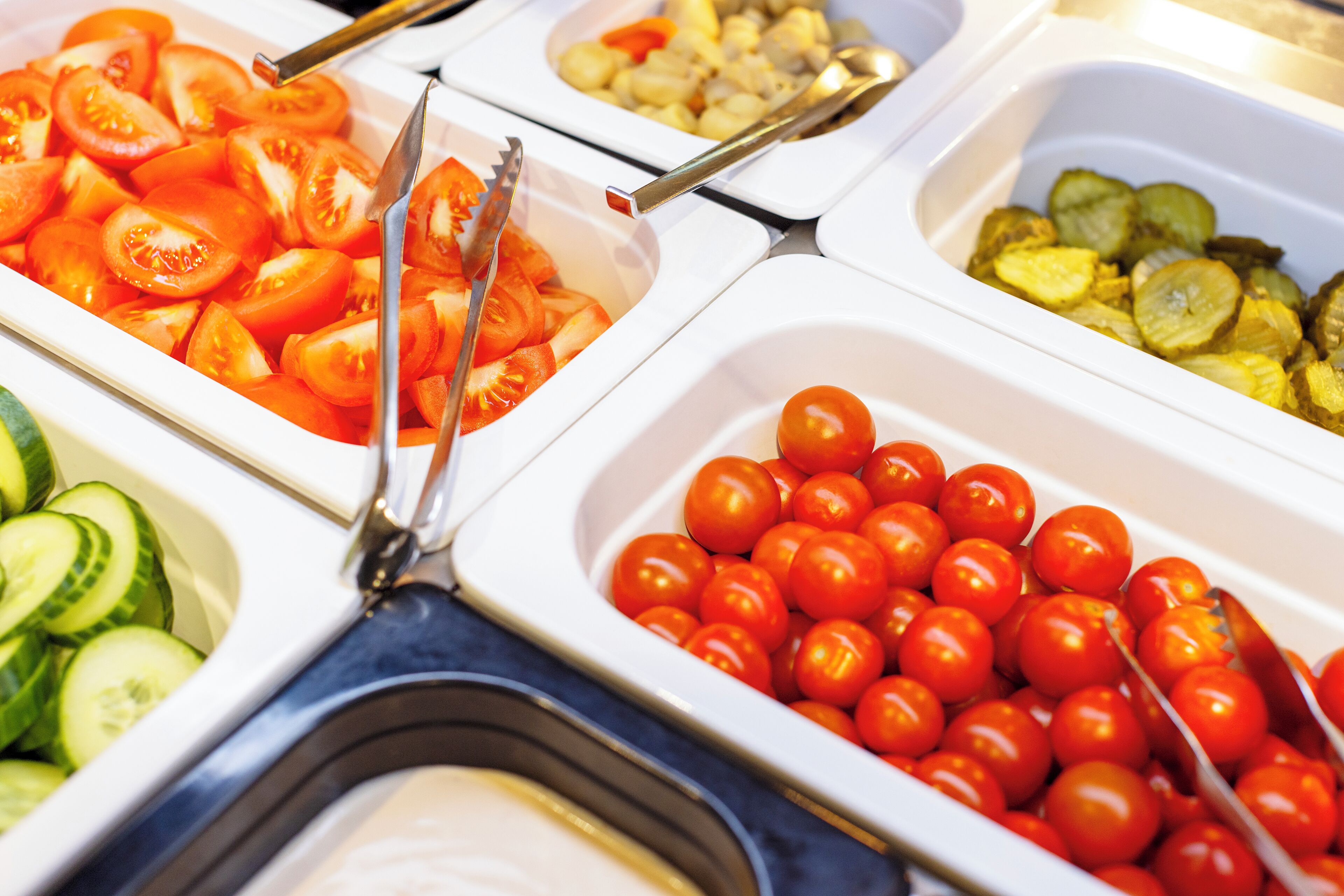 A buffet with various food items including sliced tomatoes, cucumbers, and cherry tomatoes.