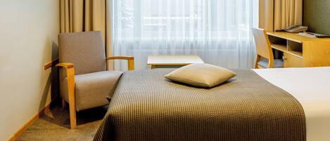 Habitación de hotel con cama, escritorio, silla, televisor y ventana con cortinas.
