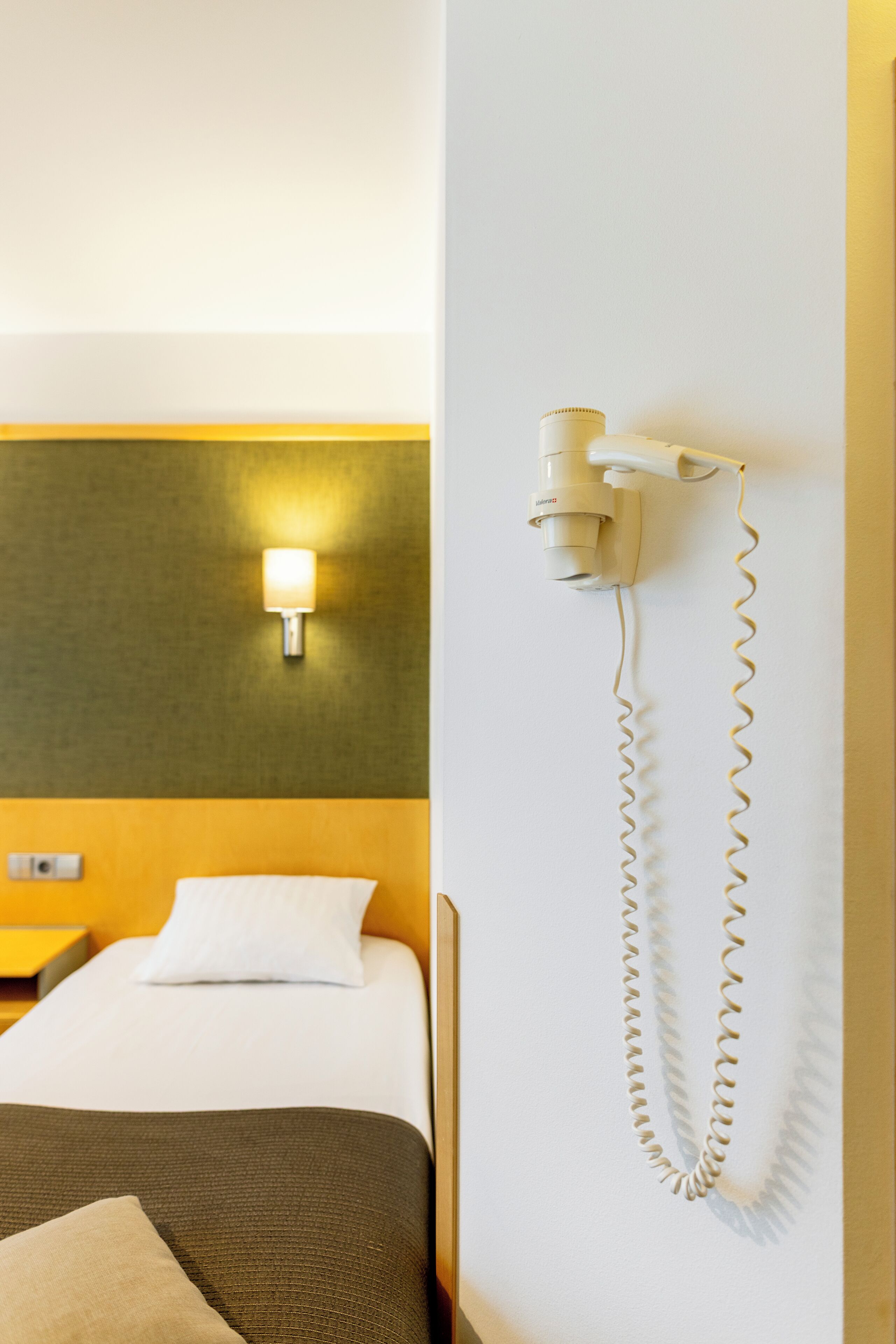 Una habitación de hotel con cama, mesita de noche, lámpara y teléfono instalado en la pared.