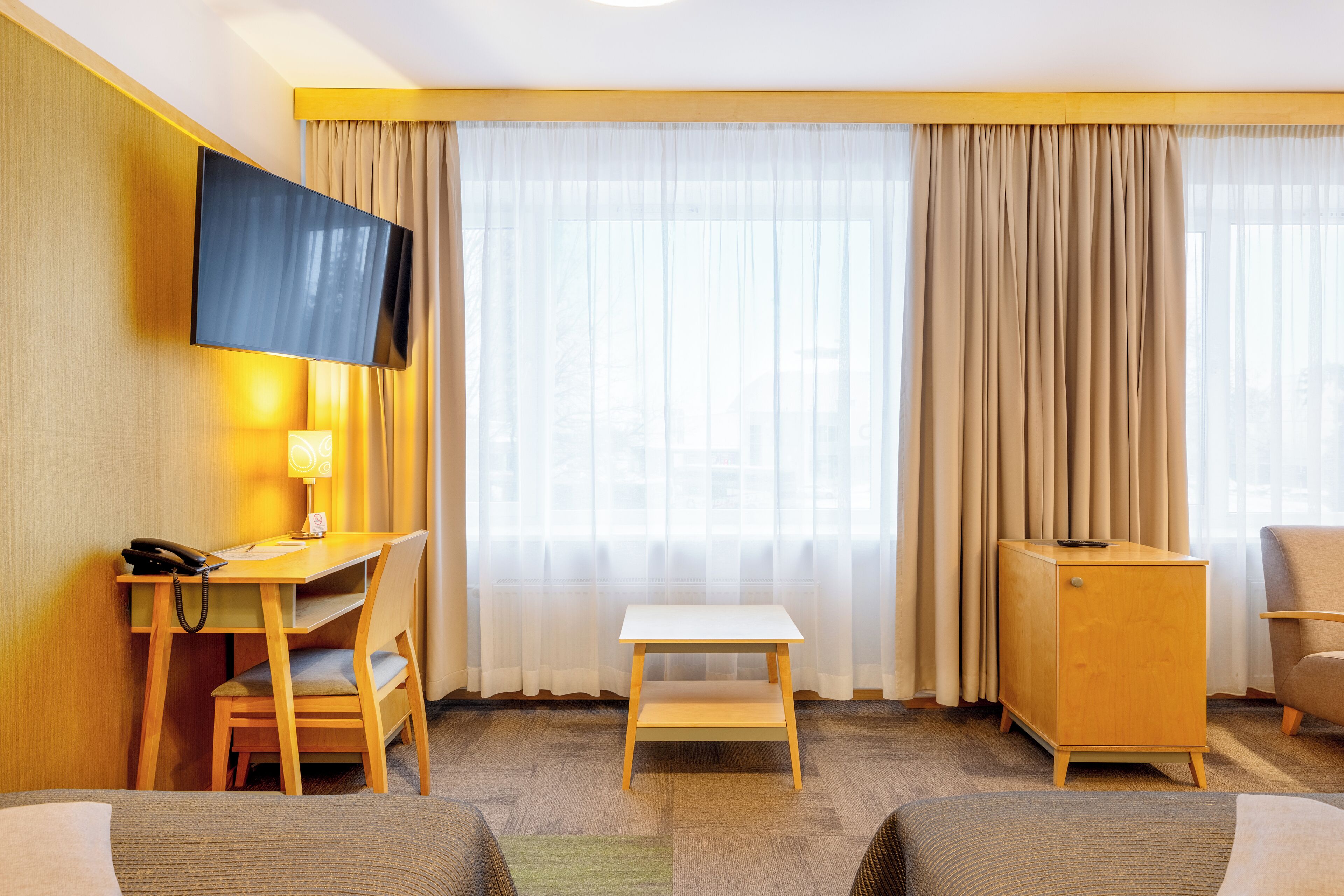 A hotel room with a desk, chair, television, and a small cabinet.