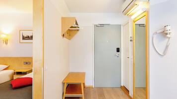 A hotel room with a bed, a small wooden table, a mirror, a wall-mounted heater, and a hairdryer.