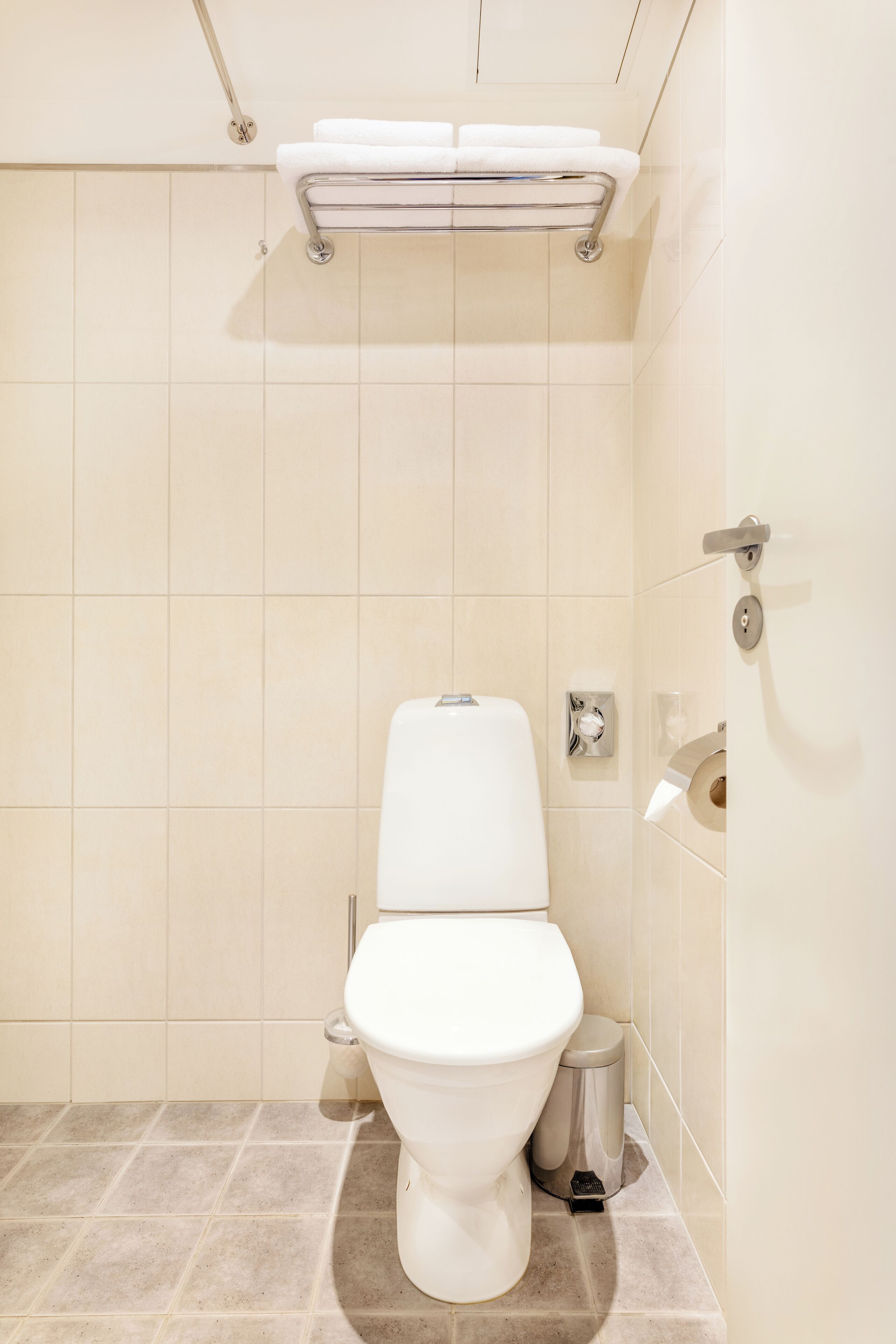 Un baño pequeño y limpio, con inodoro, un bote de basura y un toallero.
