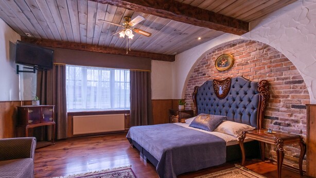 A bedroom with a large bed, wooden ceiling, brick wall, and a ceiling fan.