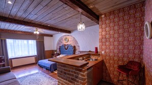 A cozy room with a wooden ceiling, a built-in kitchen with a sink, a red chair, and a patterned wall.