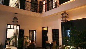 A multi-level dining area with tables set for a meal, a decorative water feature, and ambient lighting. - Riad Villa Wengé (Marrakech)