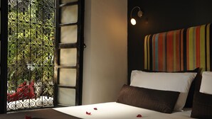 A hotel room with a bed, a window with decorative iron bars, and a colorful striped headboard. - Riad Villa Wengé (Marrakech)