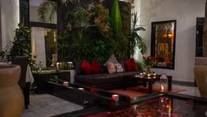 A modern living room with a sofa, red cushions, a small table with candles, and a water feature with rose petals. - Riad Villa Wengé (Marrakech)