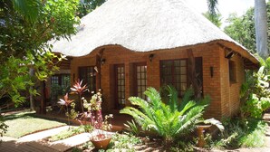 A thatched-roof house with brick walls, surrounded by lush greenery and potted plants. - Trees Too Guest Lodge (Nkomazi)