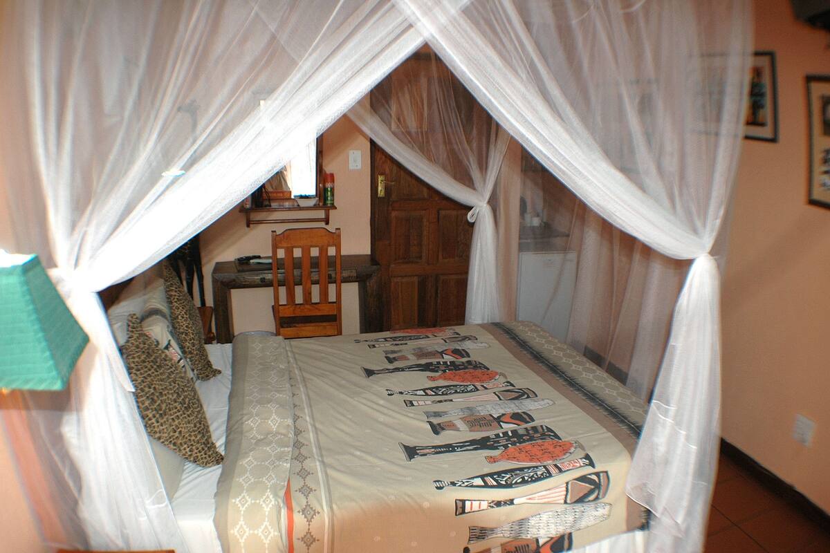 Quarto com cama coberta por um dossel, uma cadeira de madeira e uma escrivaninha com cadeira.