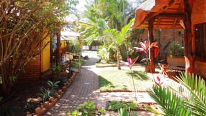 A garden pathway leading to a thatched-roof building with a brick wall and a small pool. - Trees Too Guest Lodge (Nkomazi)
