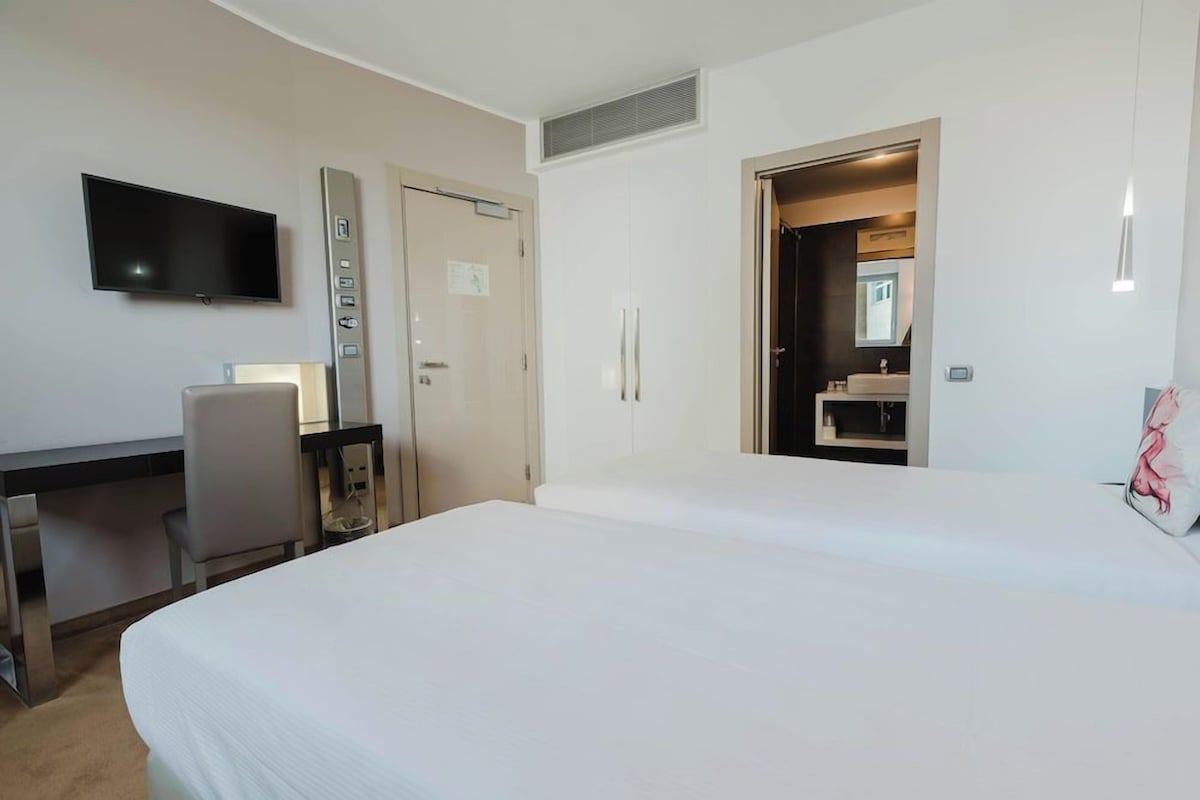 A hotel room with a bed, a desk with a chair, a television, and a bathroom visible through an open door.