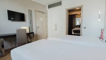 Habitación de hotel con cama, escritorio con silla, televisor, puerta y baño visible a través de una puerta abierta.