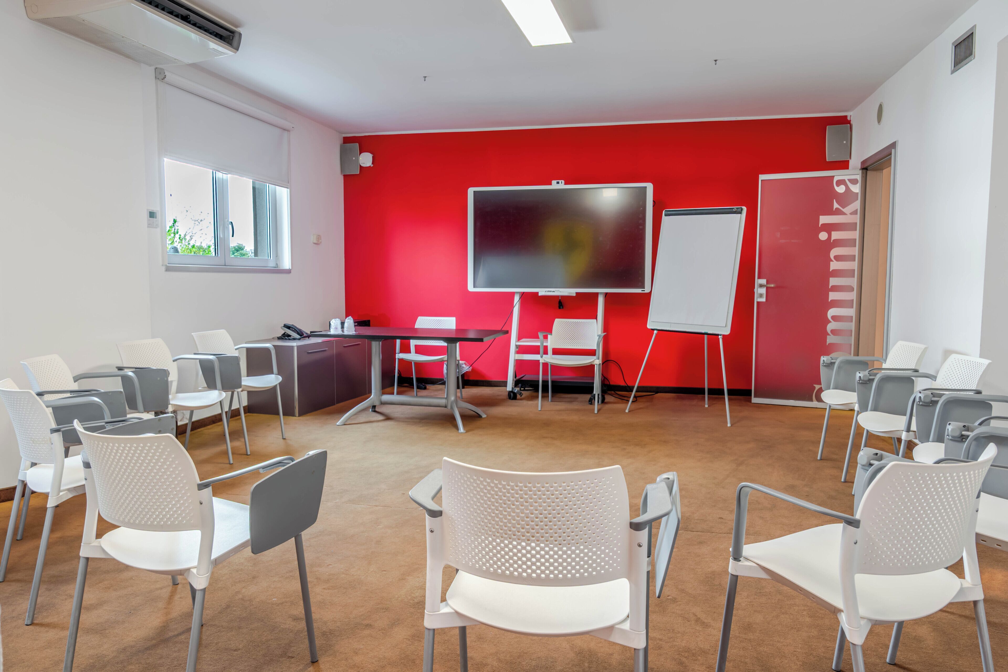 A conference room with a red wall, whiteboard, and a large screen.