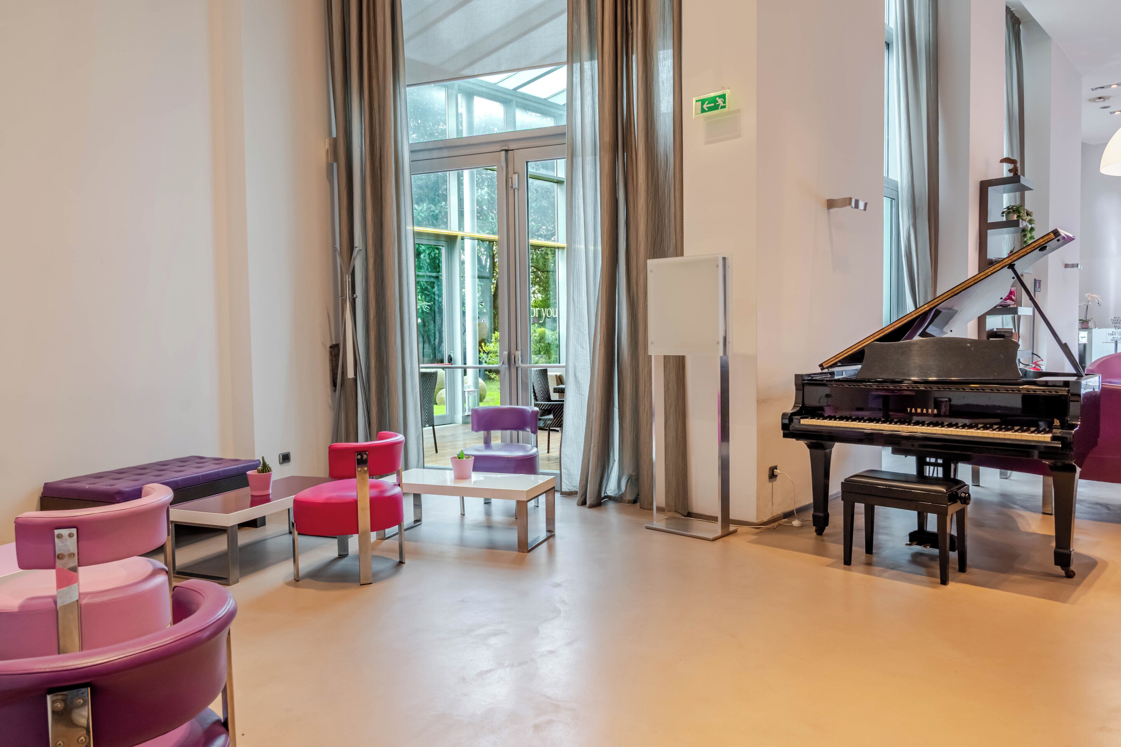 A room with a grand piano, pink seating, and a view through large windows.