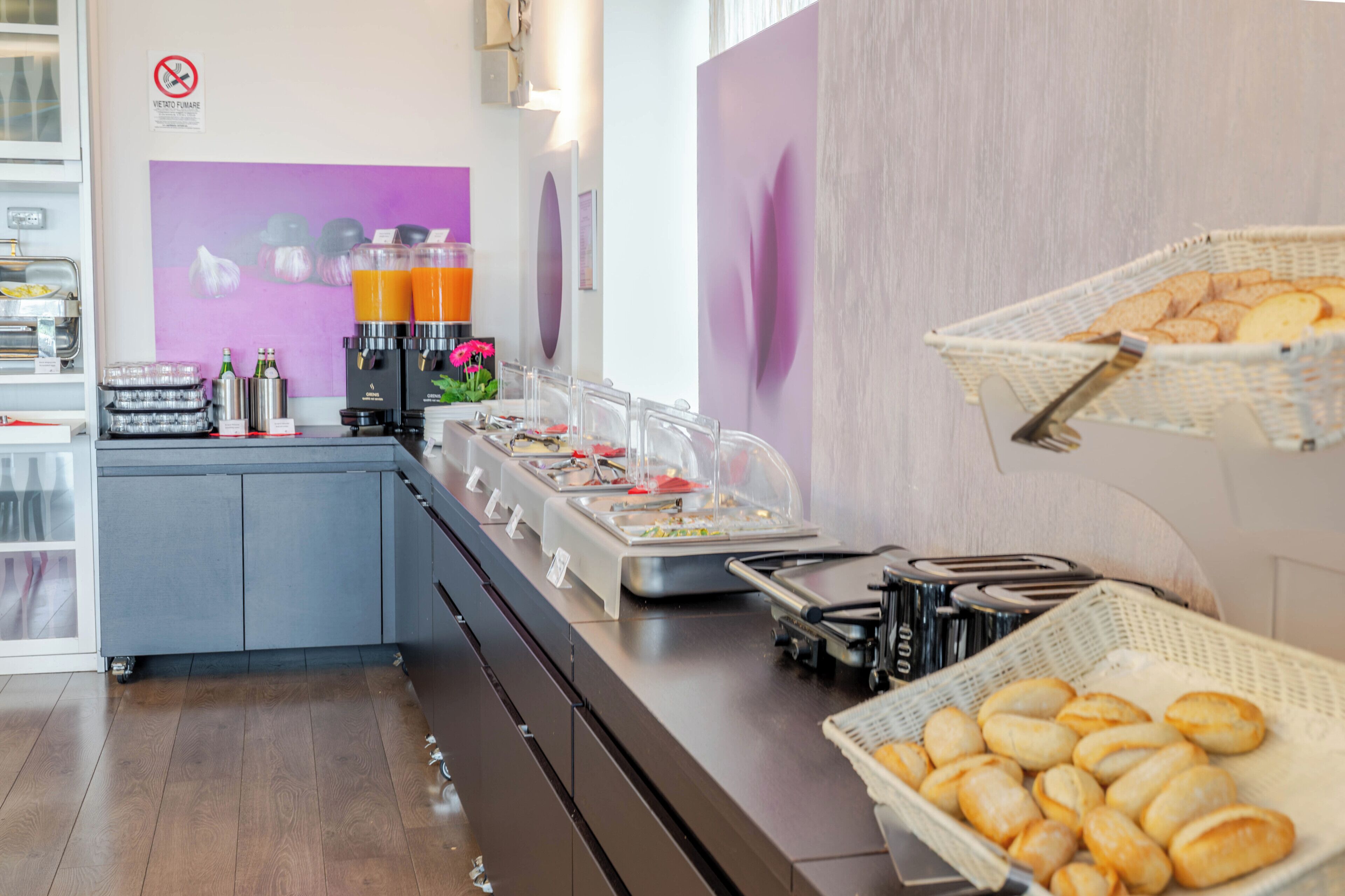 A buffet area with various food items and beverages, a no-smoking sign, and a wall with abstract art.
