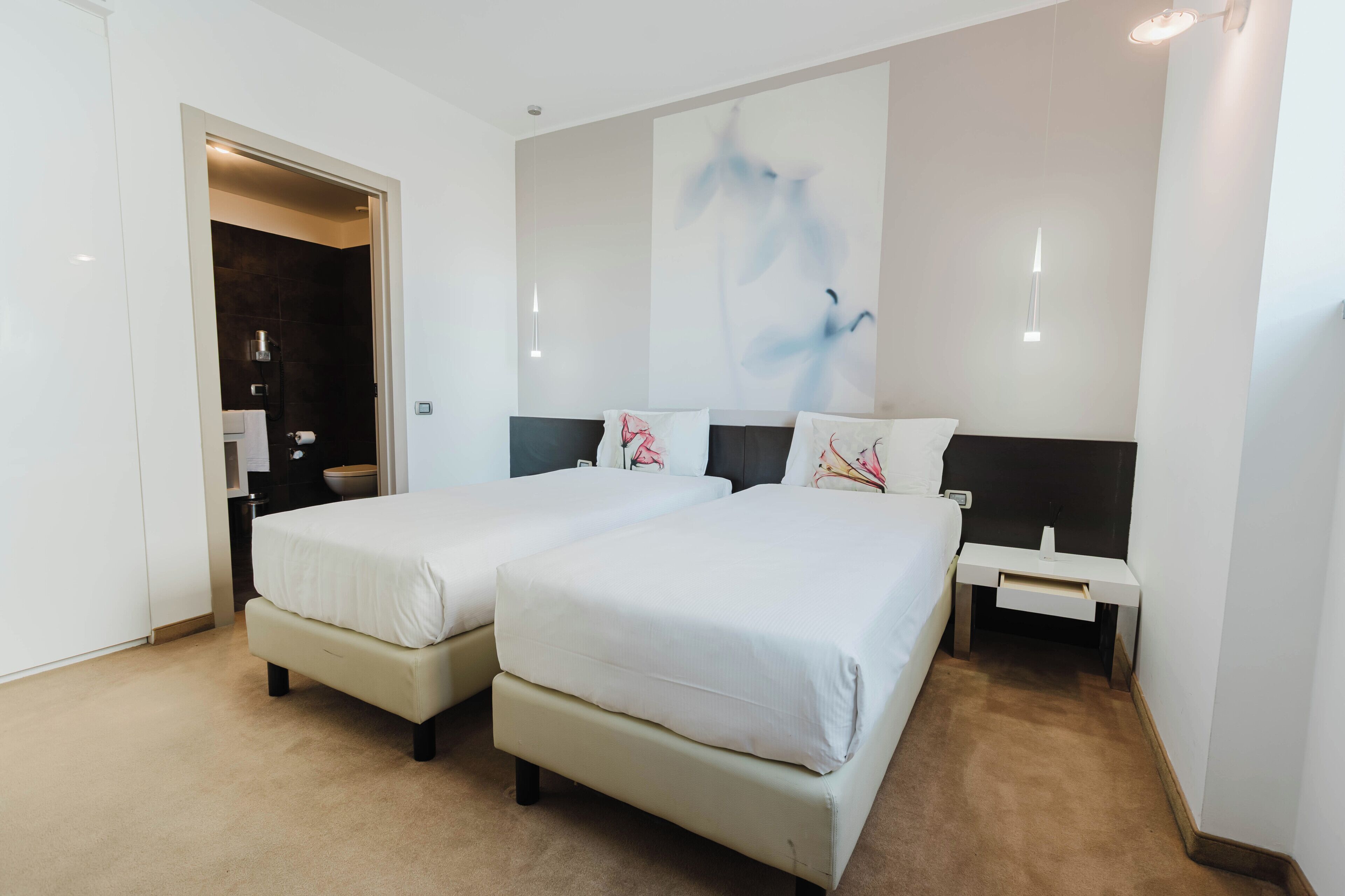 A hotel room with two beds, a small desk, and a painting on the wall.