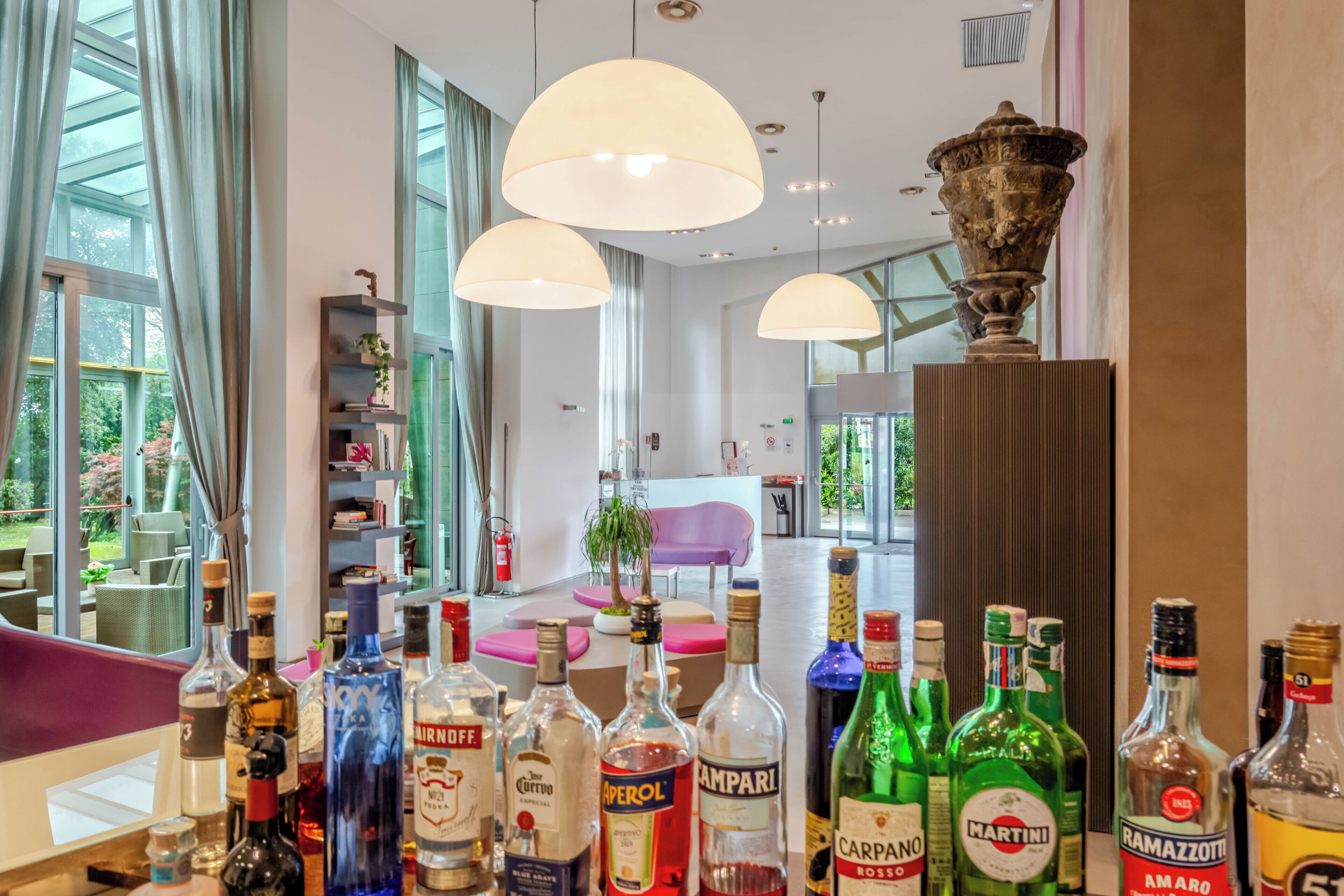 A bar area with various liquor bottles, a large decorative urn, and a modern interior with large windows and pendant lighting.