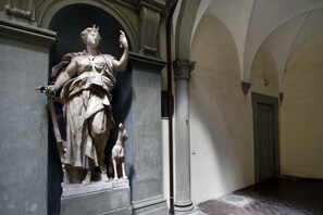 A statue of a woman holding a child in a hallway with arches and columns. - Palazzo Tolomei - Residenza d'Epoca (Florence)