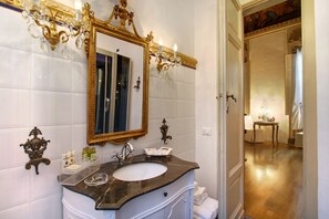 A bathroom with a marble sink, gold-framed mirror, and ornate wall sconces. - Palazzo Tolomei - Residenza d'Epoca (Florence)