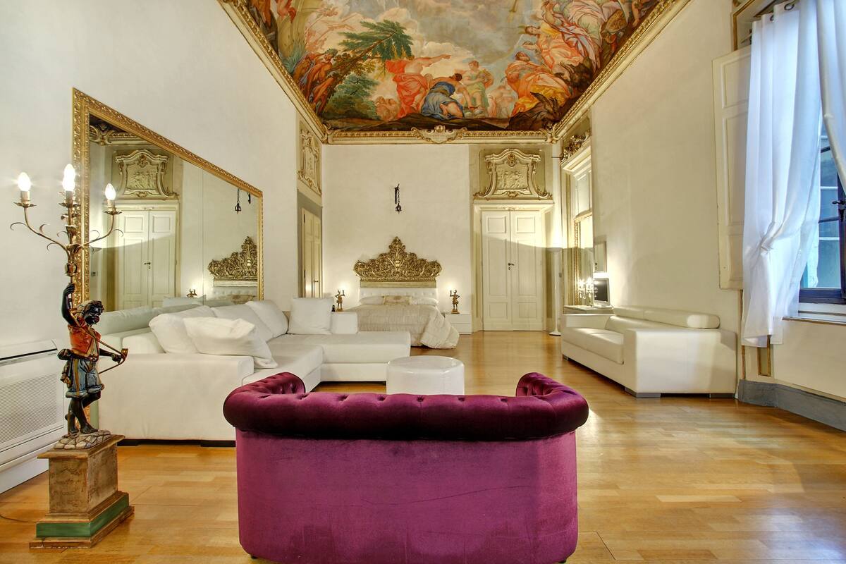 A spacious living room with a large white sofa, a purple ottoman, and a decorative statue.