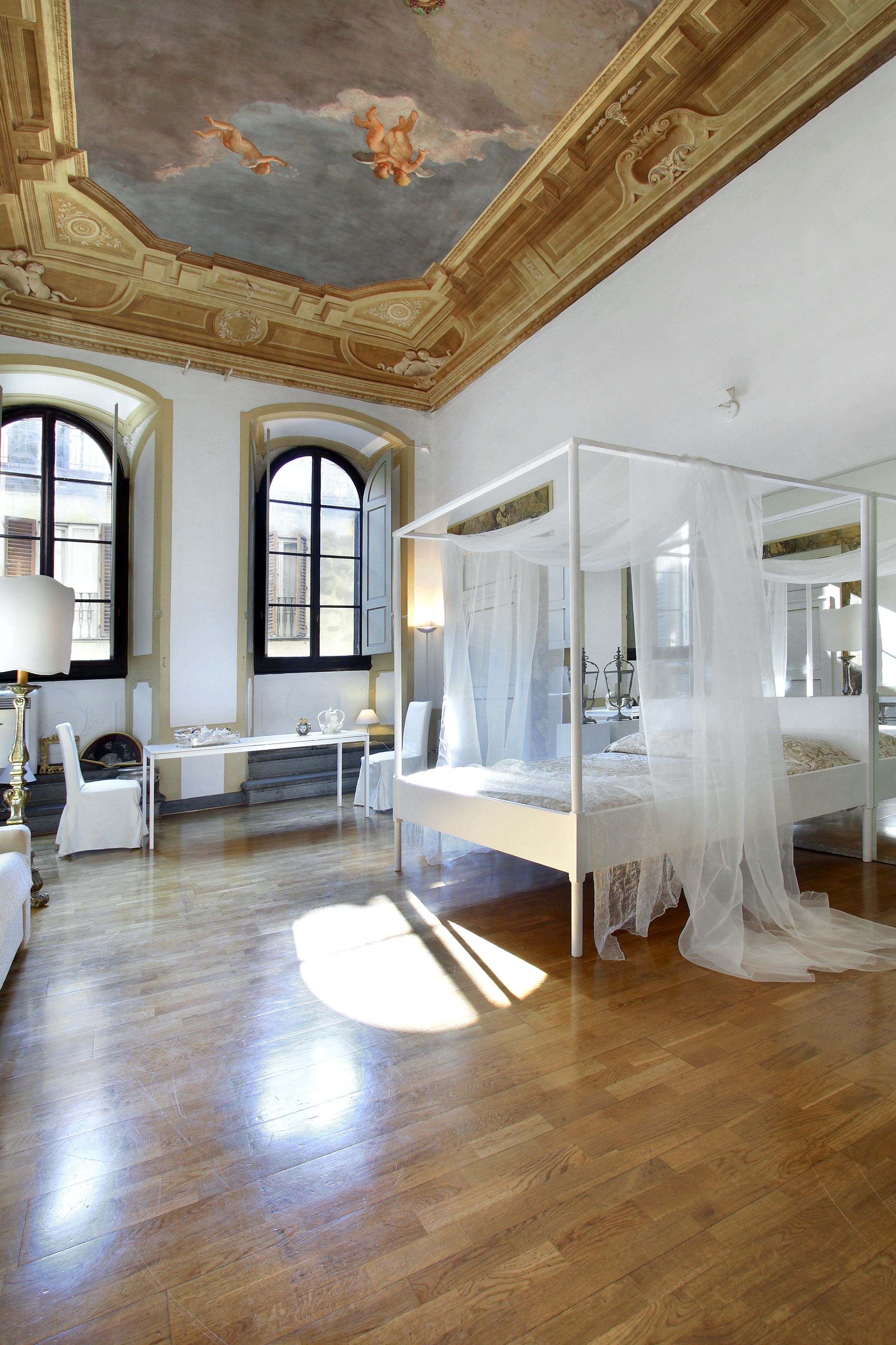 Ein geräumiges Zimmer mit einem großen Bett, einer Sitzecke mit Tisch und Stühlen sowie großen Fenstern mit Rundbögen.
