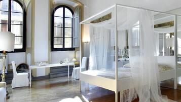 Ein geräumiges Zimmer mit einem großen Bett, einer Sitzecke mit Tisch und Stühlen sowie großen Fenstern mit Rundbögen.