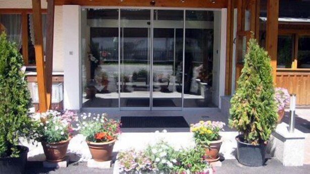 Un espace extérieur abrité, doté d’une porte vitrée donnant sur un coin salon. On y trouve des plantes en pot et une petite table avec des chaises.