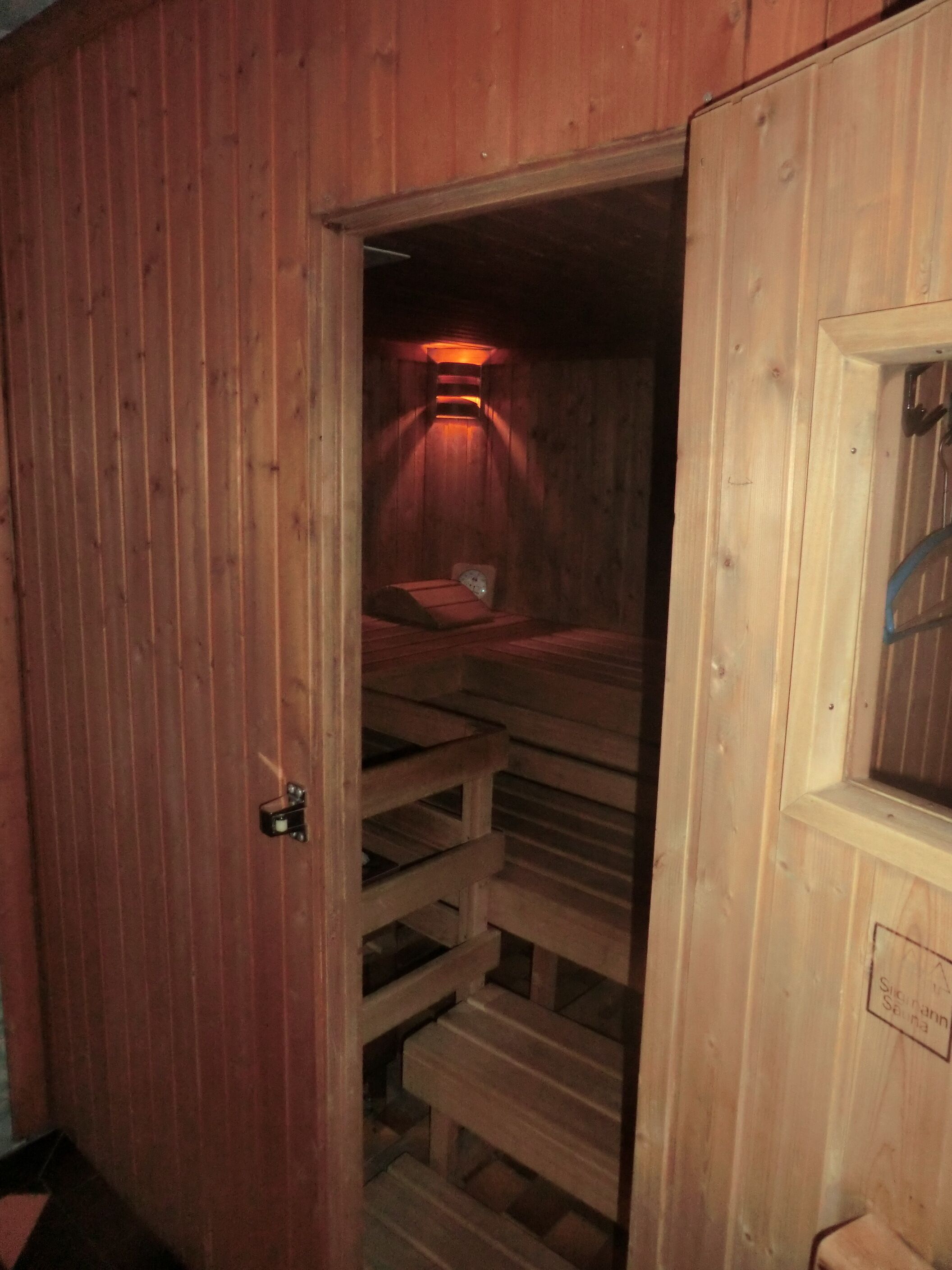 Un sauna aux murs en bois, doté d’une porte, d’un banc et d’une banquette.