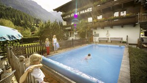Une piscine avec une terrasse en bois et un bâtiment sur lequel est apposée une enseigne.
