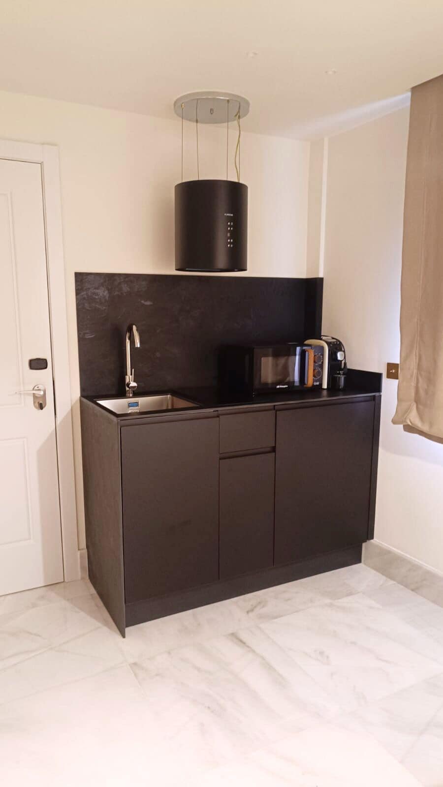 A compact kitchen with a dark countertop, a microwave, a toaster, and a modern light fixture.