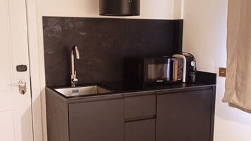 A compact kitchen with a dark countertop, a microwave, a toaster, and a modern light fixture.