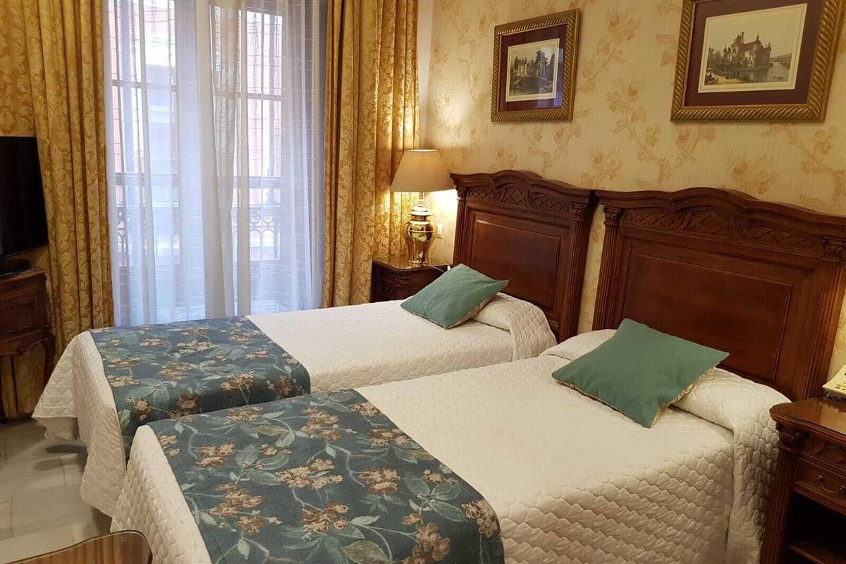 A hotel room with two beds, a TV, a lamp, and a window with curtains.