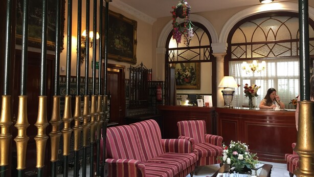 A lobby with a reception desk, striped sofas, a piano, and a chandelier.