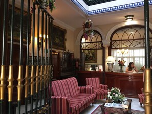 A lobby with a reception desk, striped sofas, a piano, and a chandelier. - Hotel Europa (Seville)