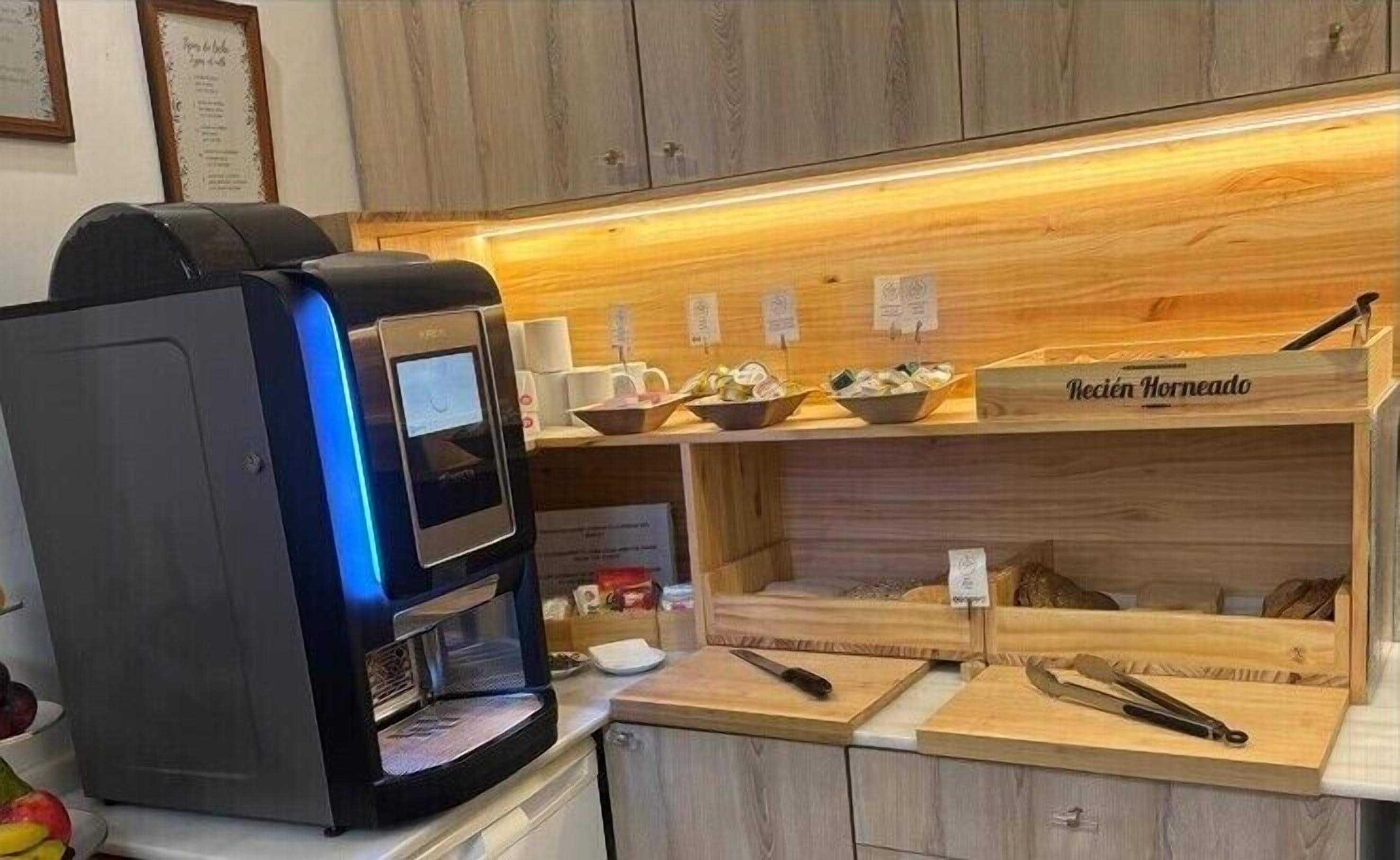 Uma máquina de café, um balcão de madeira com a placa 'Recien Horneado' e diversos utensílios de cozinha.