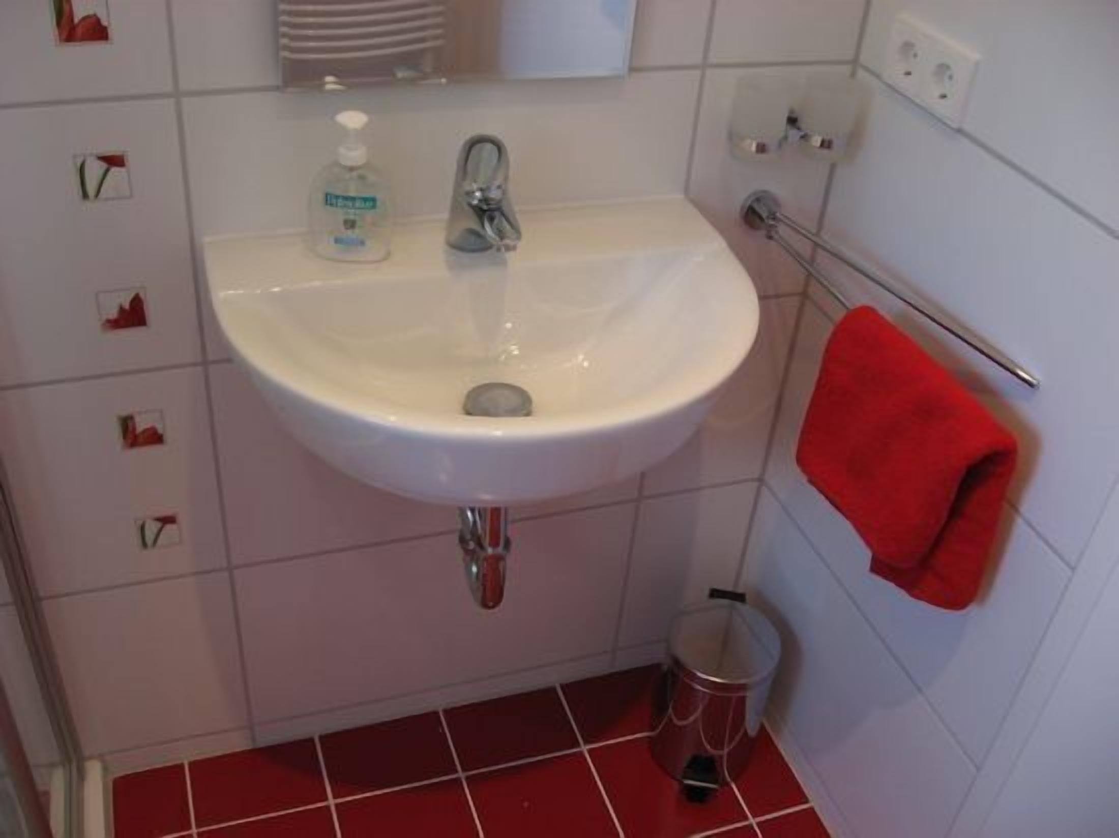 A bathroom with a white sink, a red towel, and a trash can.