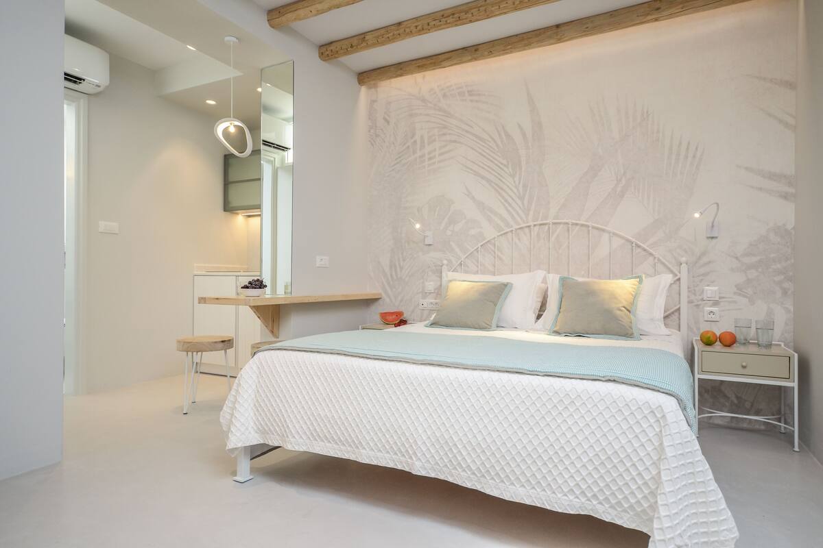 A bedroom with a bed, bedside tables, a nightstand, a mirror, and a wall with a palm tree design.