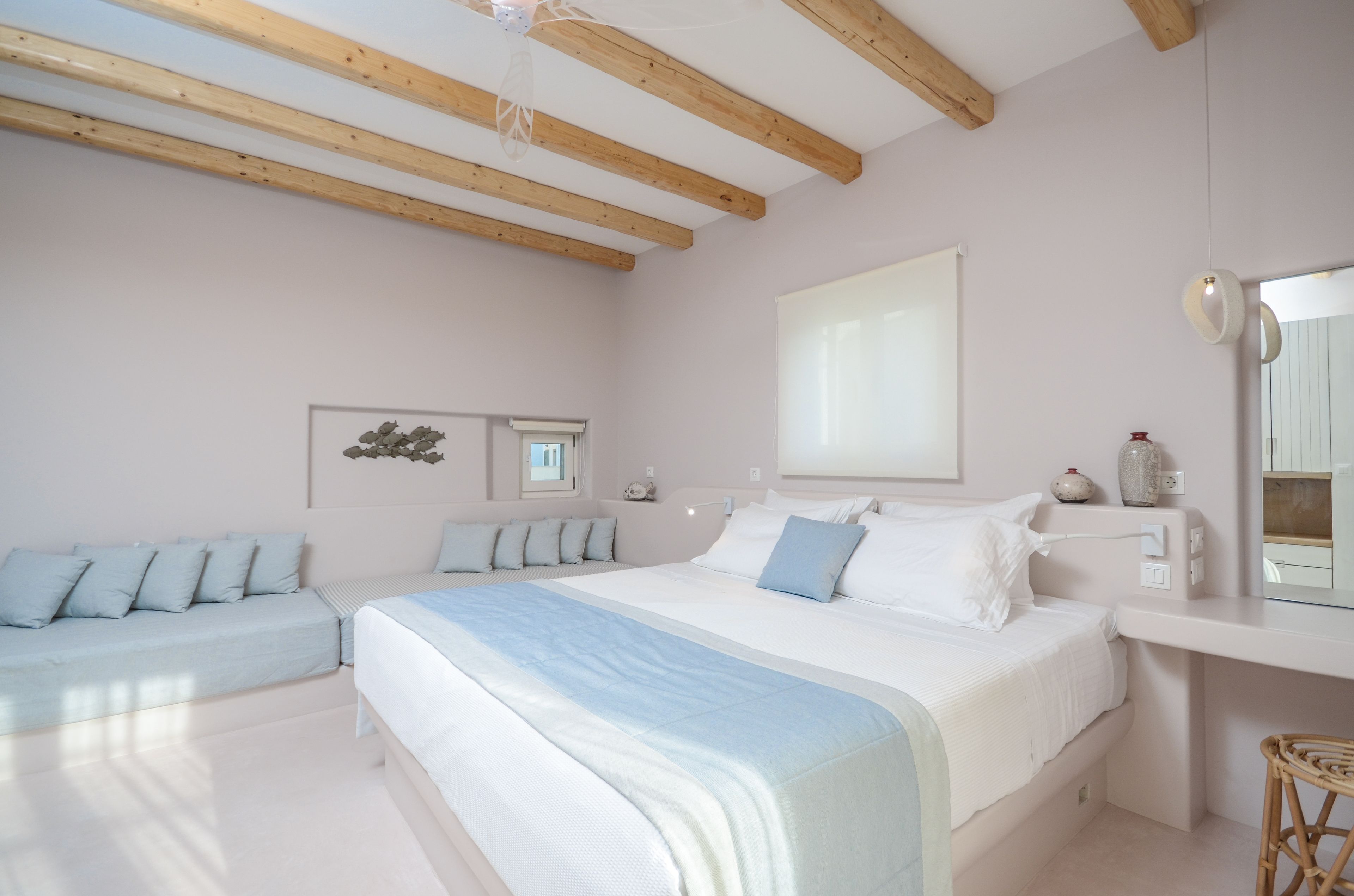 Een slaapkamer met een groot bed, een kleiner bed, een nachtkastje, een spiegel en een wandplank.
