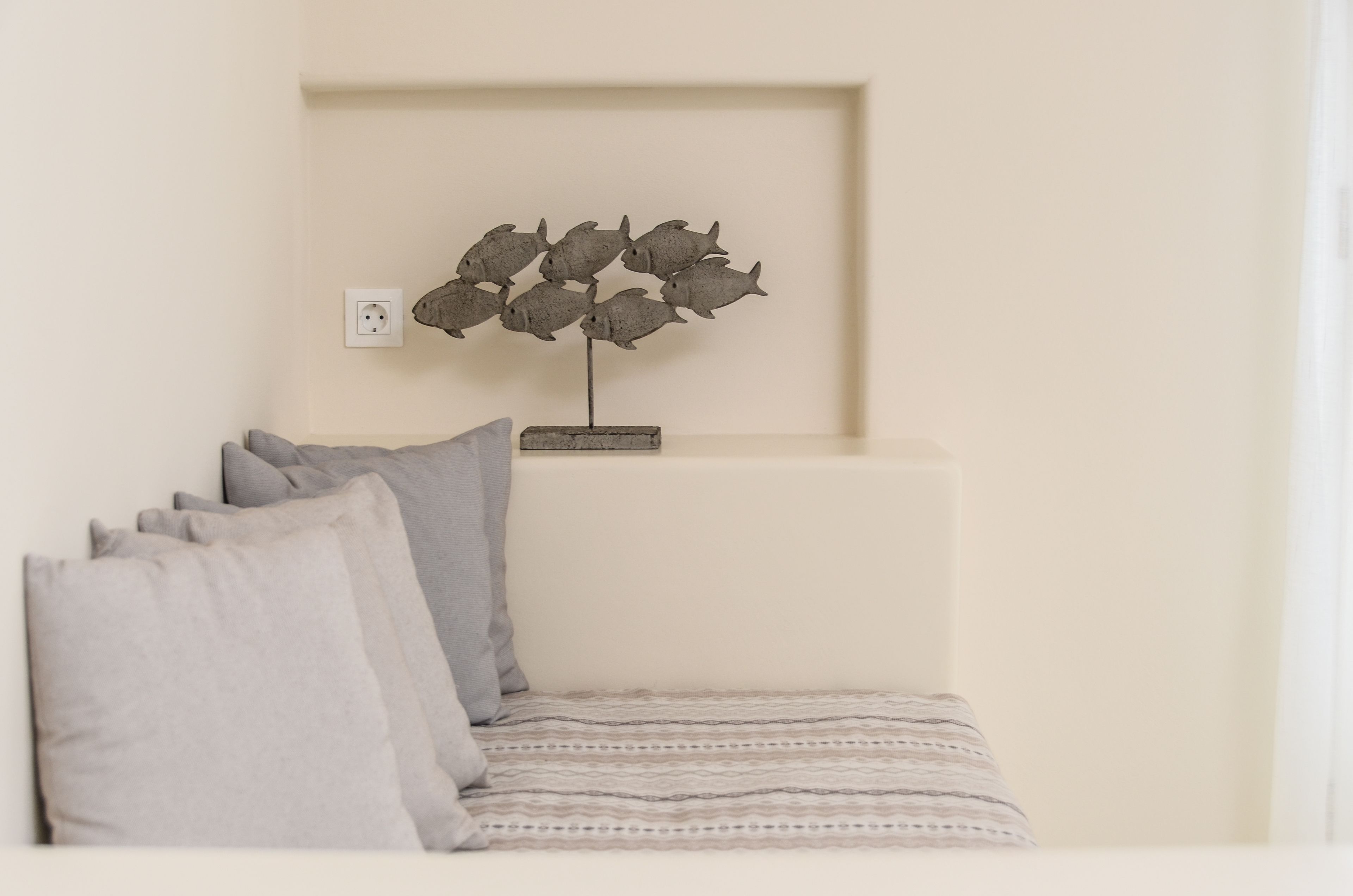 Habitación minimalista con una cama, almohadas y una escultura de pez decorativo colgado en la pared.