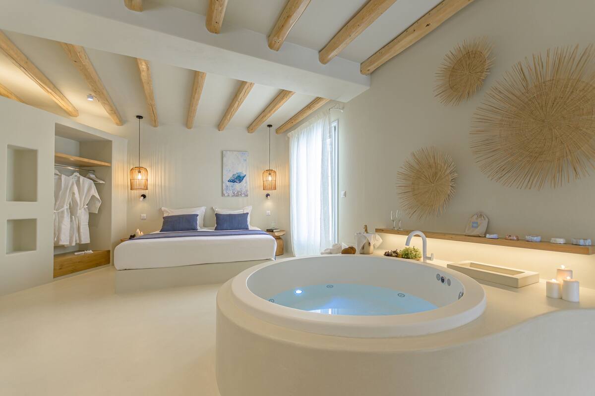 A modern bedroom with a large bathtub, a bed with blue bedding, and a wooden ceiling.