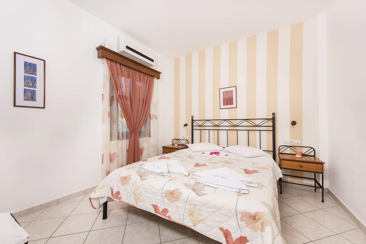 A neatly made bed with floral bedding, a bedside table with a lamp, a nightstand, and a framed picture on the wall.
