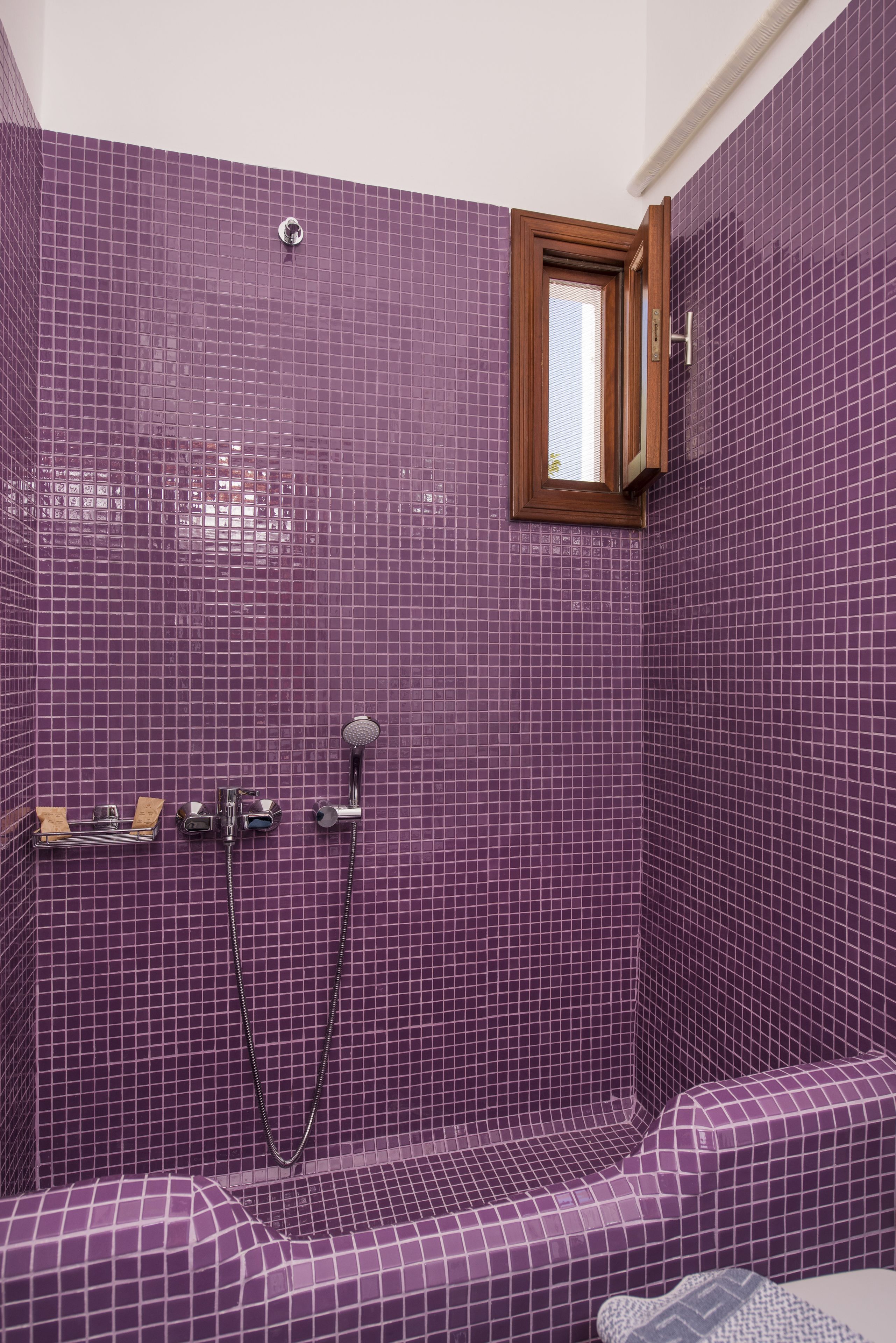 Ein Badezimmer mit violetten Fliesen, einer Dusche und einem Fenster.