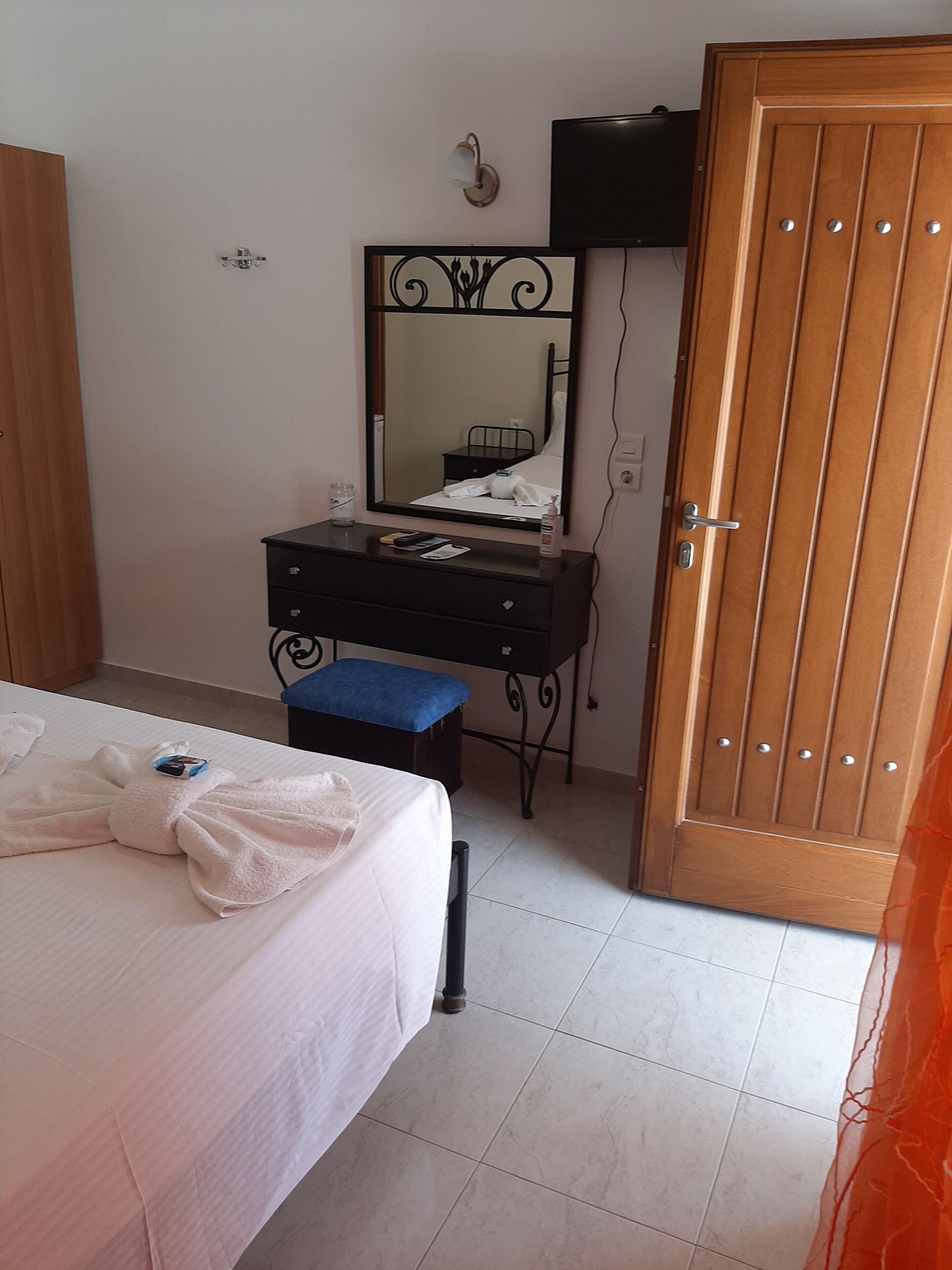 A hotel room with a bed, a bedside table, a mirror, a wooden wardrobe, and a bathroom door.