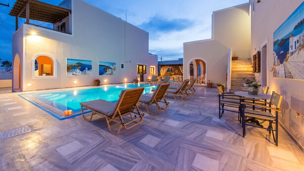 A poolside area with lounge chairs, a staircase, and a view of the sea. - Villa Voula (Santorini)