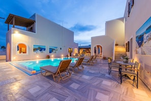 A poolside area with lounge chairs, a staircase, and a view of the sea. - Villa Voula (Santorini)