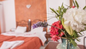 A bed with a white and orange bedspread, a vase with flowers, and a wooden headboard. - Villa Voula (Santorini)