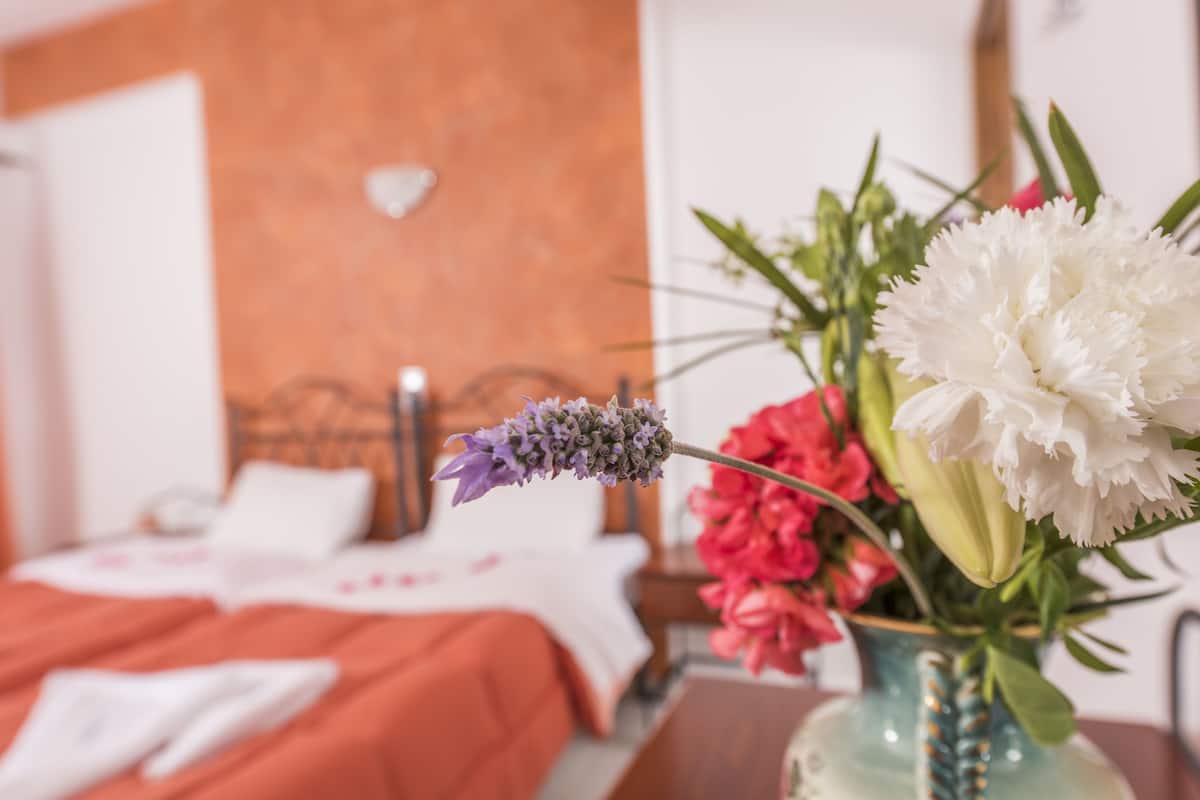 A bed with a white and orange bedspread, a vase with flowers, and a wooden headboard.